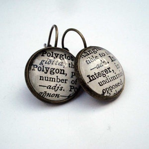 Peut inclure: Une paire de boucles d'oreilles de couleur bronze avec des cabochons en verre. Les cabochons en verre présentent du texte noir provenant d'une page de dictionnaire. Le texte sur la boucle d'oreille gauche se lit comme suit : "Polyglot glotta, th Polygon, p number of -adjs. Po non". Le texte sur la boucle d'oreille droite se lit comme suit : "angin tible to t -adr. In Integer, in undiminis Opposed".
