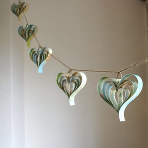 A handmade garland of heart shaped created from strips of vintage atlas paper, the hearts are hanging on rustic twine and the colour is blue green.