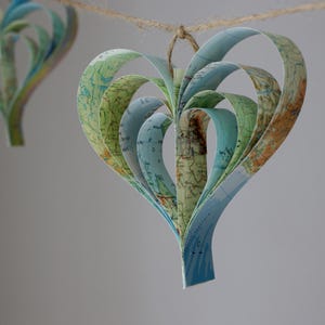 A handmade garland of hearts created from strips of vintage atlas paper, the hearts are hanging on rustic twine and the colour is blue green.