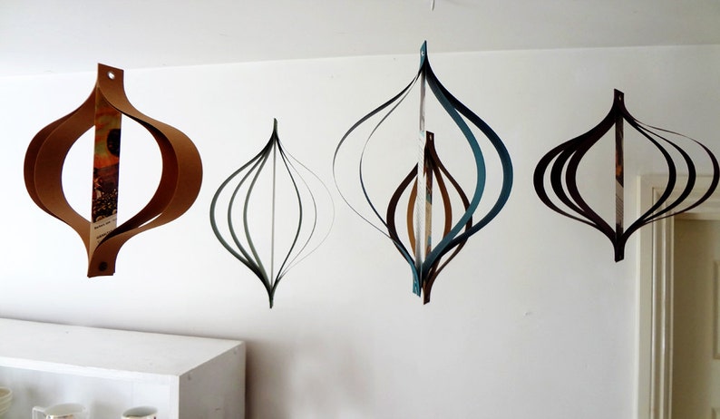 May include: Four paper ornaments hanging from the ceiling. The ornaments are made of paper and are in the shape of a teardrop. The ornaments are in different colors, including brown, black, and blue.