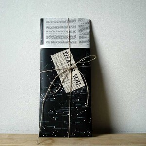An example of the packaging that the garland will be packed in. It is a tall thin envelope made from a page of an atlas showing text and star diagrams.