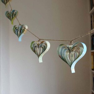 A handmade garland of heart shape created from strips of vintage atlas paper, the hearts are hanging on rustic twine and the colour is blue green.