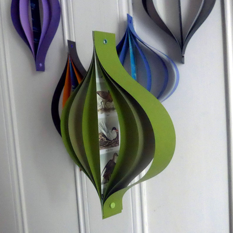 May include: A green paper ornament with a bird design. The ornament is made of multiple layers of paper that are folded and overlapped to create a three-dimensional shape.