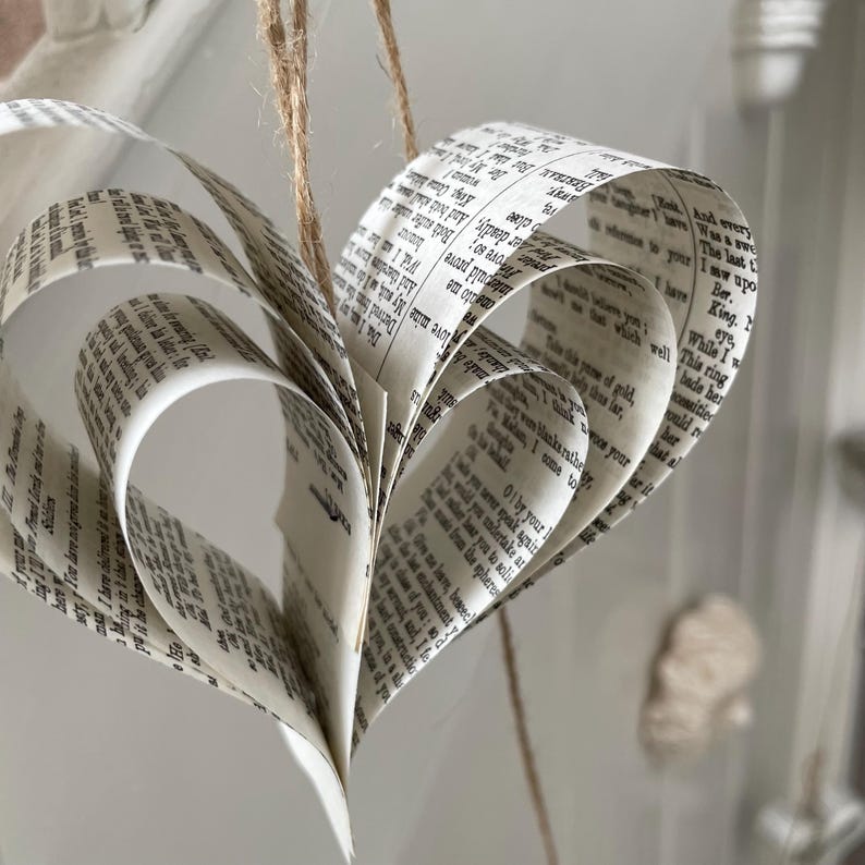 A handmade garland of hearts created from strips of vintage shakespeare's plays, the hearts are hanging on rustic twine and the colour of the paper is off white with black text.