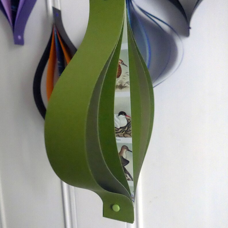 May include: A green paper ornament with a layered design. The ornament features a series of images of birds, including a tern, a hummingbird, and a kingfisher.