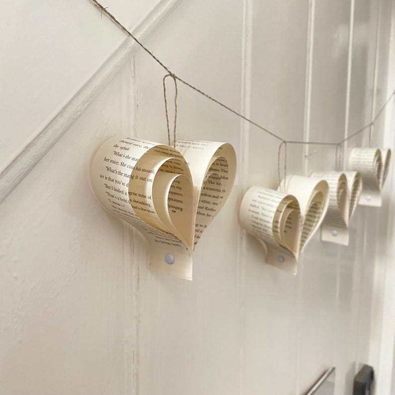 A handmade garland of heart shapes created from strips of book pages, the hearts are hanging on rustic twine and the colour is cream.