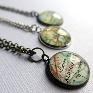 May include: Three necklaces with round glass pendants featuring vintage maps. The pendants are silver and bronze colored. The map on the bottom pendant shows the text "Moulton" and "NEWMARKET".