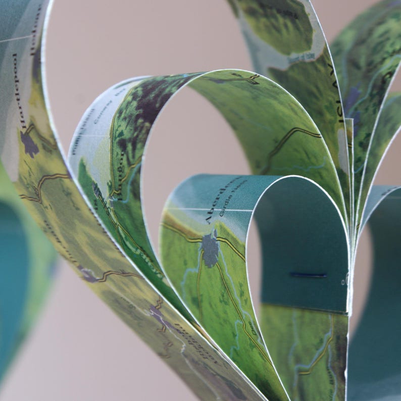A close up view of a handmade garland of heart shapes created from strips of vintage atlas paper, the hearts are hanging on rustic twine and the colour of the paper is blue green.