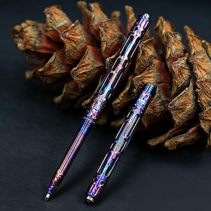 Könnte beinhalten: Ein Metallstift und die dazugehörige Kappe mit einem irisierenden, wärmeanodisierten Finish in den Farben Tiefblau, Violett und Bronze. Der Schaft und die Kappe haben ein skelettiertes Design mit länglichen Ausschnitten und einem strukturierten, gerippten Griffbereich.