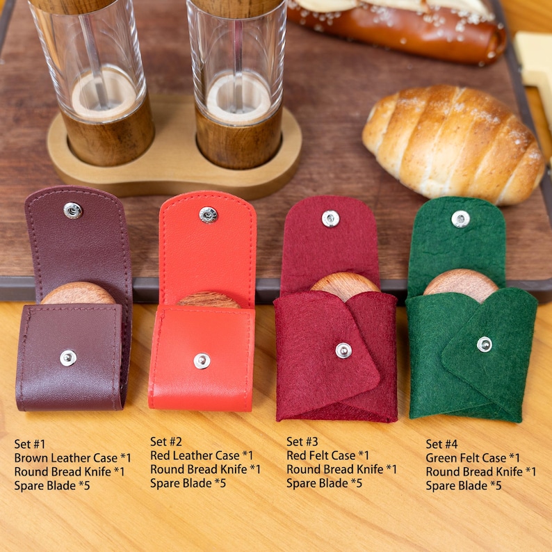 Peut inclure: Quatre ensembles de couteaux &agrave; pain avec des lames de rechange, chacun dans un &eacute;tui de couleur diff&eacute;rente : cuir marron, cuir rouge, feutre rouge et feutre vert. Pr&eacute;sent&eacute;s sur une surface en bois, avec un bretzel et du pain en arri&egrave;re-plan.