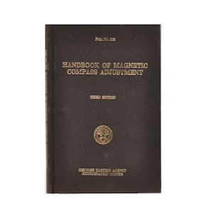 May include: A black book titled "Handbook of Magnetic Compass Adjustment" with the words "Third Edition" and "Defense Mapping Agency Hydrographic Center" printed in gold.