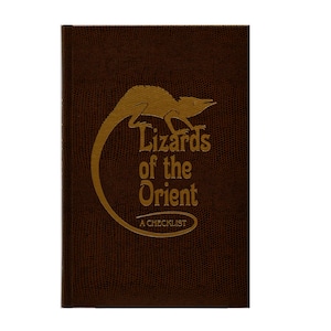 Può includere: Un libro marrone con un'illustrazione di lucertola dorata sulla copertina. Il titolo è "Lizards of the Orient: A Checklist".