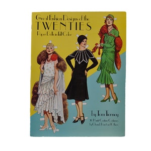 Può includere: Un libro di bambole di carta vintage con tre donne vestite con la moda degli anni '20. La copertina del libro è gialla e blu con il titolo "Great Fashion Designs of the TWENTIES Paper Dolls in Full Color" e l'autore "by Tom Tierney".