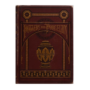May include: A burgundy book with gold lettering and decorative accents. The title of the book is "Pottery and Porcelain".