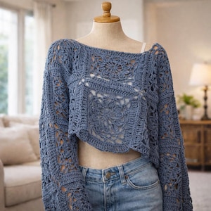 May include: A blue crochet top with long sleeves and an open, floral design. The cropped sweater is displayed on a mannequin and paired with blue jeans. The top features an off-the-shoulder neckline and a unique, openwork pattern.