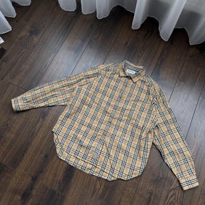 May include: A long-sleeved button-down shirt in a classic plaid pattern. The shirt features a tan base with black, white, and red stripes. The shirt is made of a soft, comfortable material.