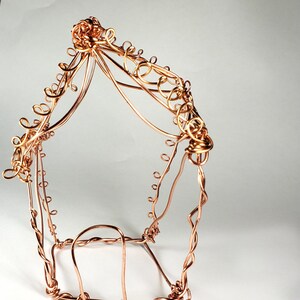 May include: A copper wire sculpture of a house with a decorative, ornate design. The house is made of twisted and curled wire, creating a delicate and intricate pattern.