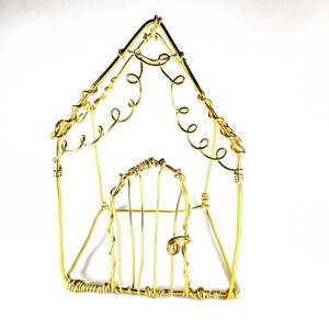 May include: A gold wire sculpture of a house with a detailed, ornate design. The house has a door and a roof with a decorative pattern.