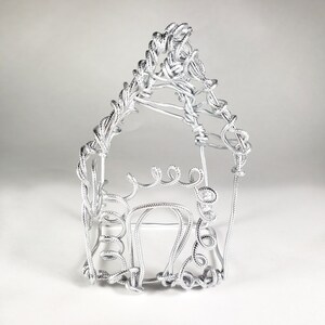 May include: A silver wire sculpture of a house with a pointed roof. The sculpture is made of twisted wire and has a simple, minimalist design.