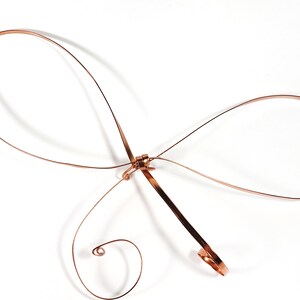 May include: A copper wire sculpture in the shape of a butterfly. The sculpture is made of a single piece of wire that is bent and twisted to create the wings and body of the butterfly.
