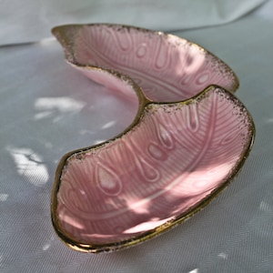 May include: A pink, divided serving dish with a gold trim. The dish has a feather-like pattern embossed on the interior. The dish is made of ceramic or porcelain and is likely vintage.