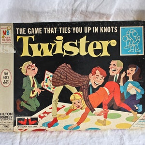 以下が含まれることがあります： ツイスターというゲームのビンテージゲームボックス。箱には、ゲームをしている人々のカラフルなイラストが描かれており、ゲームの名前が大きな黄色の文字で書かれています。箱のテキストには、「あなたを結びつけるゲーム」と書かれています。
