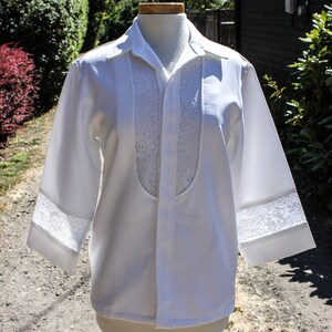 May include: A white long-sleeved shirt with a lace trim around the collar and cuffs. The shirt has a button-up front and a lace panel down the center front.