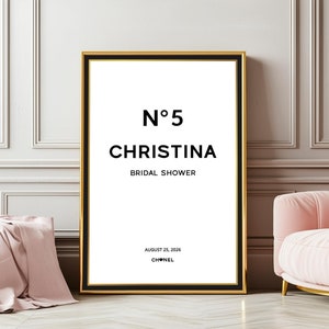 Könnte beinhalten: Ein schwarz-weißes druckbares Schild mit goldener Umrandung, mit dem Text "N°5 Christina Bridal Shower August 25, 2026 CHANEL" in einem minimalistischen Design.