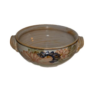 May include: A ceramic bowl with a wide rim and two handles. The bowl is beige with a floral pattern in shades of pink, blue, and green. The interior of the bowl is a lighter beige color.