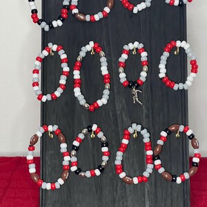 Peut inclure: Un ensemble de 10 bracelets en perles sur le thème du football. Les bracelets sont faits de perles blanches, rouges, noires et brunes. Certains bracelets ont des perles argentées et un charme de football.