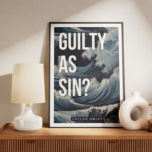May include: A framed vertical wall art print featuring a dark blue ocean wave illustration with white sea foam. The text GUILTY AS SIN? is printed in large white capital letters, with TAYLOR SWIFT in smaller white text at the bottom of the print.