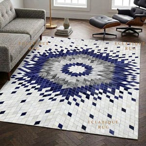 Pode incluir: Um tapete retangular com um padrão geométrico de diamantes em tons de azul marinho, cinza e branco. O design irradia a partir de um diamante central branco, com quadrados menores criando um efeito de mosaico. O texto ECLATIQUE RUG é visível.