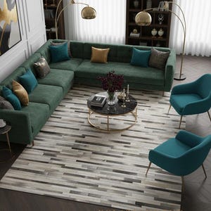 Könnte beinhalten: Ein modernes Wohnzimmer mit einem großen, grünen Ecksofa, das mit türkisfarbenen und goldenen Kissen geschmückt ist. Ein runder Couchtisch aus schwarzem Marmor steht auf einem gemusterten Teppich. Zwei türkisfarbene Sessel und goldene Bogenlampen vervollständigen den Raum.