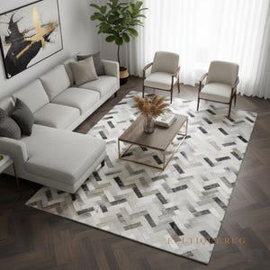 May include: A contemporary living room scene with a light grey sofa, two armchairs, and a coffee table. A patterned rug with a herringbone design in grey, black, and white tones covers the floor. An abstract painting hangs on the wall.