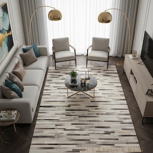 May include: A modern living room featuring a light gray sofa, two armchairs, and a rectangular rug with a striped pattern in shades of gray and beige. Two gold arc lamps illuminate the space. A round coffee table and a TV console complete the decor.
