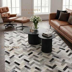 May include: A rectangular area rug featuring a repeating herringbone pattern composed of individual tiles in shades of white, grey, and black. The text ECLATIQUE RUG is visible in gold lettering at three different locations on the rug surface.