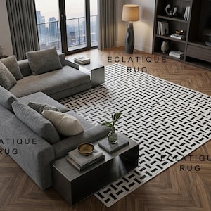 Pode incluir: Uma sala de estar moderna com um sofá cinza, um tapete estampado e uma mesa lateral. O tapete tem um design geométrico em preto e branco. A sala é bem iluminada com luz natural e um candeeiro de pé.