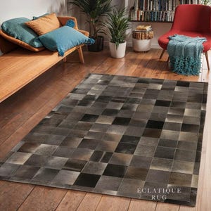 Puede incluir: Una alfombra rectangular con un diseño de patchwork en tonos grises, marrones y negros. La alfombra está hecha de cuadrados y rectángulos, creando un patrón geométrico. El texto "ECLATIQUE RUG" es visible en la esquina inferior derecha.