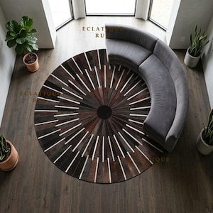 May include: A large circular area rug featuring a radial pattern of dark brown, black, and white leather strips arranged in a sunburst design with a solid black center circle. The text ECLATIQUE RUGS is visible in gold lettering on the rug surface.