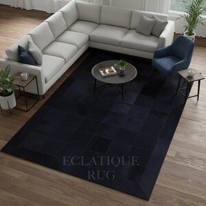 May include: A large, dark blue rug with a geometric pattern, placed in a living room setting. The rug features a grid design and a border. The text "ECLATIQUE RUG" is visible on the rug. The room includes a light gray sectional sofa and a blue armchair.