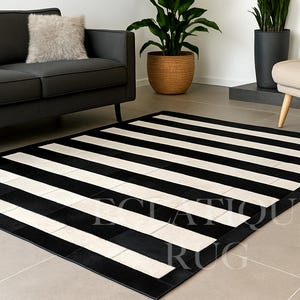 Puede incluir: Una alfombra rectangular con llamativas rayas blancas y negras. La alfombra tiene un borde negro y está colocada sobre un suelo de baldosas de color neutro. El diseño a rayas es una pieza llamativa para un salón.