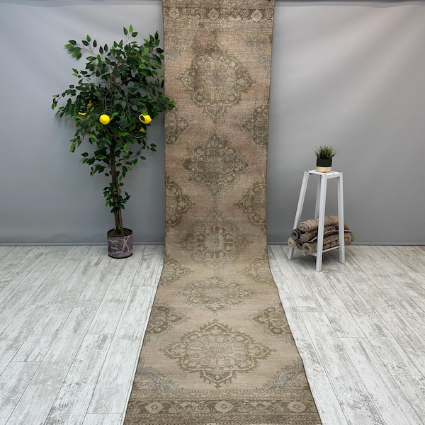 May include: A long, rectangular, vintage rug with a faded, light pink background and a brown, floral pattern. The rug is laid out on a light wood floor.