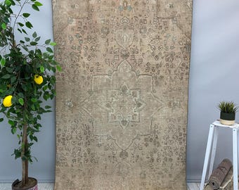 Puede incluir: Una alfombra grande y rectangular de estilo vintage con un diseño de medallón central y intrincados patrones florales en tonos beige, marrón y verde descolorido. La alfombra tiene un aspecto desgastado, con desgaste visible, lo que aumenta su encanto antiguo.