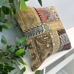 May include: A square, patchwork pillow with a vintage, distressed aesthetic. The pillow features a variety of rectangular and square patches in shades of brown, beige, red, and blue. The design includes geometric and floral patterns.