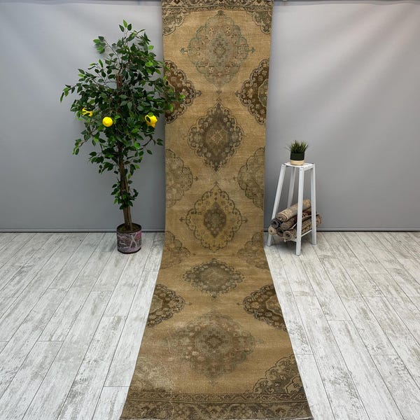 May include: A long, beige runner rug with a traditional Persian design in shades of brown and green. The rug has a fringed edge and is made of wool.