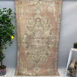 May include: A vintage Turkish rug with a faded pink and cream colour scheme. The rug has a traditional geometric pattern with intricate details. The rug is in good condition and would be a beautiful addition to any home.