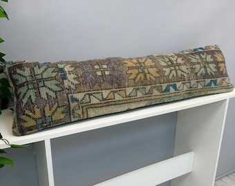 Peut inclure: Un long coussin lombaire rectangulaire doté d'une housse en textile tissé avec un motif géométrique répétitif dans des tons sourds de brun, vert sauge, jaune moutarde et bleu profond. Le tissu présente un aspect texturé et vintage.