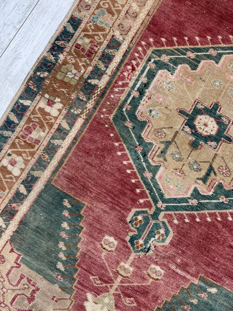 May include: Close-up of a vintage rug with a geometric design. The rug features a central field of deep red, bordered by teal and tan patterns. The intricate details include floral and geometric motifs.