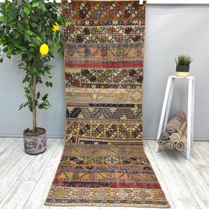 May include: A long, rectangular, vintage rug with a patchwork design. The rug features a variety of colors including red, brown, beige, and blue. The rug has a distressed look, with visible wear and tear, adding to its antique charm.
