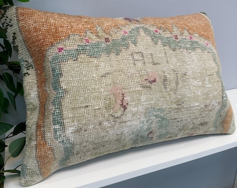 May include: A rectangular throw pillow featuring a woven textile cover with a faded pattern in shades of orange, sage green, and cream. The center displays a decorative border with small pink accents and the text ALI 17 embroidered in dark thread.